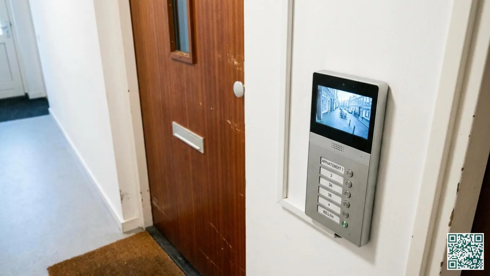 Modern video-intercom paneel naast appartementsdeur met scherm en belknoppen in een schone portiekhal