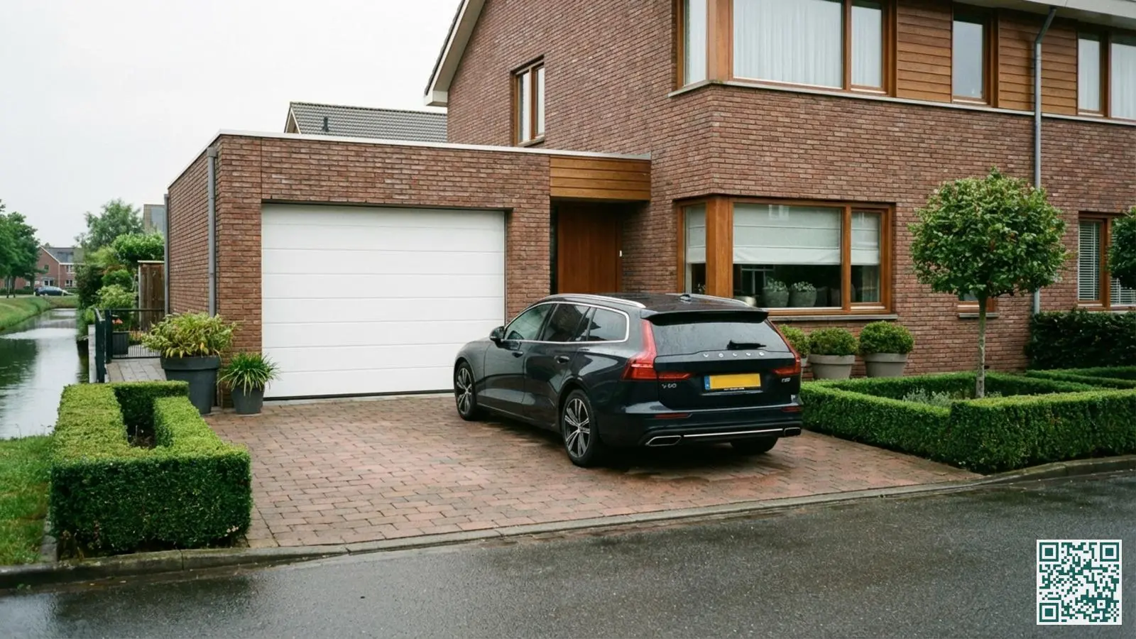 Moderne witte sectionaaldeur van een aangebouwde garage bij een Nederlands woonhuis met auto op de oprit