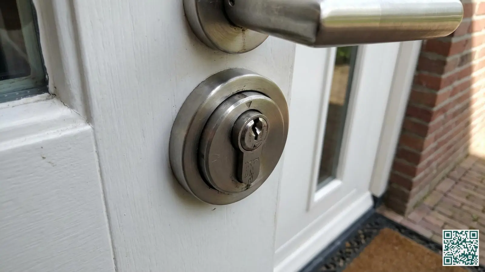 Modern veiligheidsbeslag met kerntrekbeveiliging gemonteerd op een witte houten voordeur met roestvrijstalen rozet